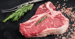 Raw porterhouse steak on a black surface with salt and rosemary from John Mull’s Meats