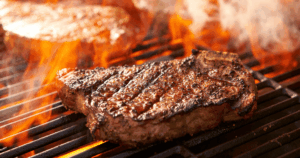 Grilling steak sizzling on a hot grill with flames and smoke at John Mull’s Road Kill Grill
