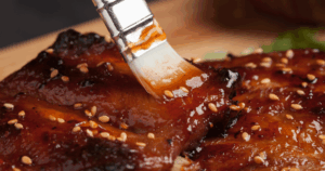BBQ sauce being brushed onto ribs with sesame seeds for a sweet and tangy glaze