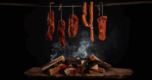 Smoked meats including sausages and cuts of pork hanging above a smoldering fire