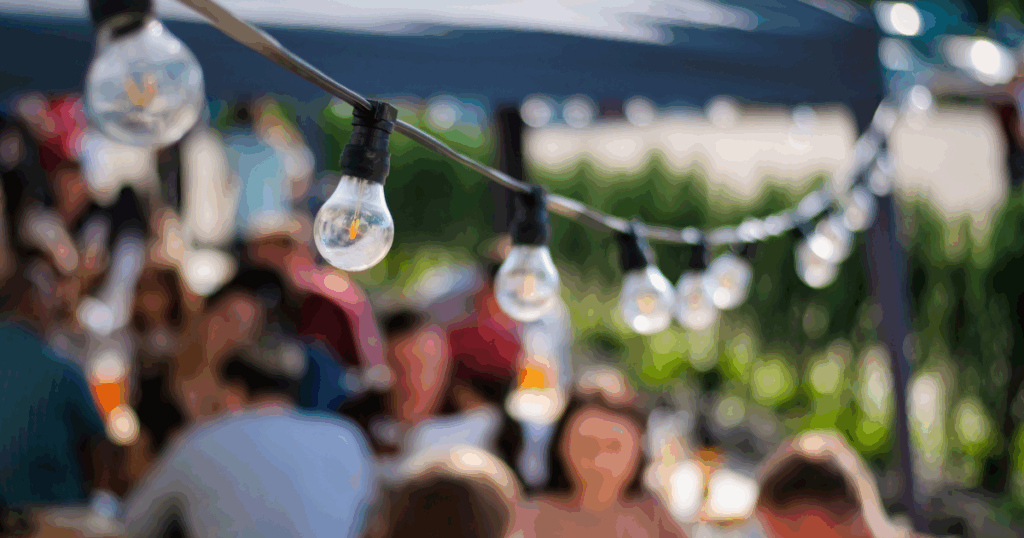 String lights above a vibrant outdoor community gathering, symbolizing connection and togetherness