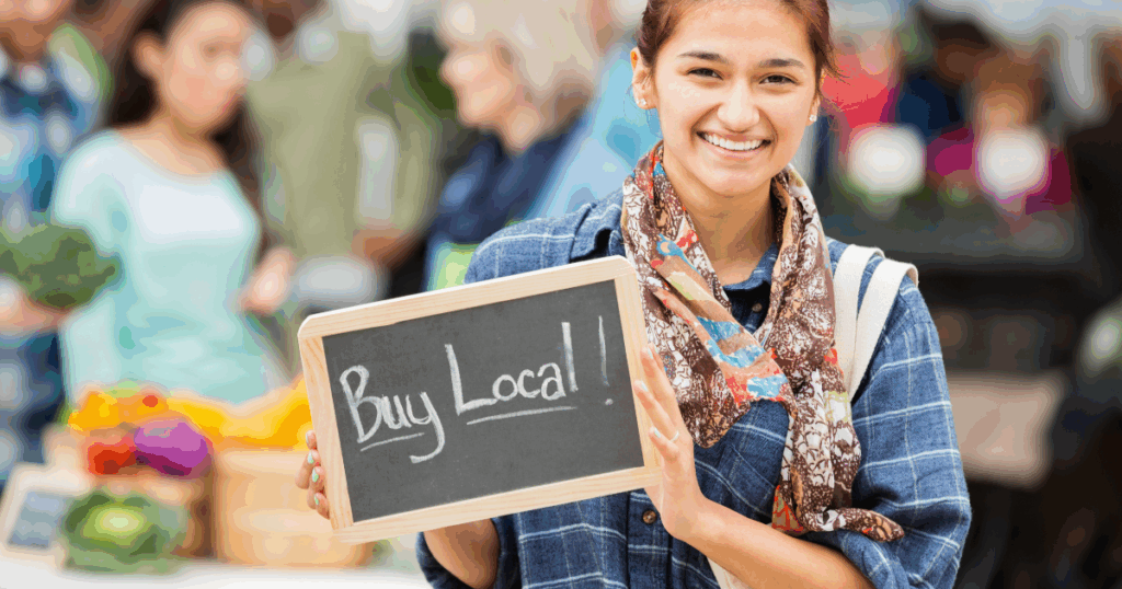 Smiling woman holding a “Buy Local” sign at a farmers market
