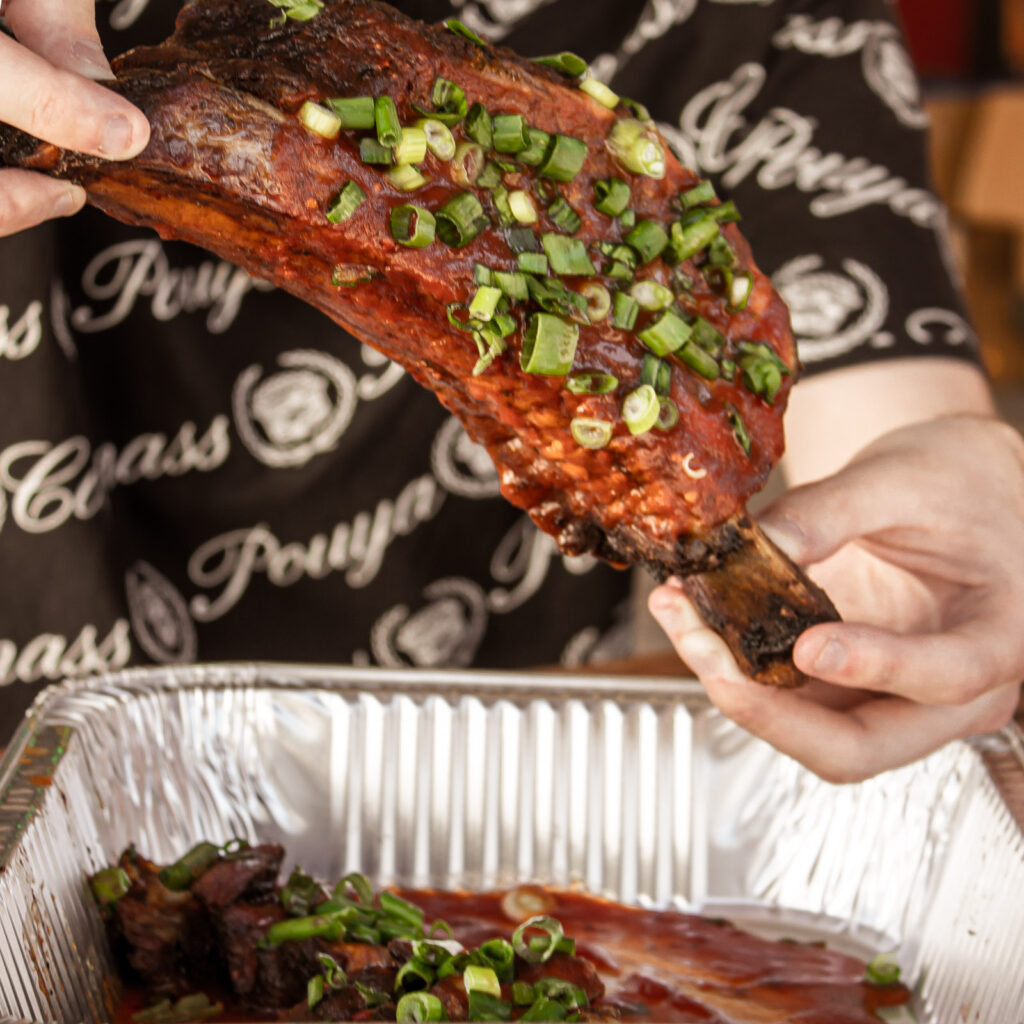 This image showcases one of John Mull’s signature BBQ rib styles, beautifully seasoned, glazed with sauce, and topped with fresh green onions. Photographed at the Road Kill Grill in Las Vegas, it captures the rich color and texture that define the restaurant’s regional BBQ variety and flavor. Ideal for illustrating articles on BBQ styles across the USA or seasonal menu features.