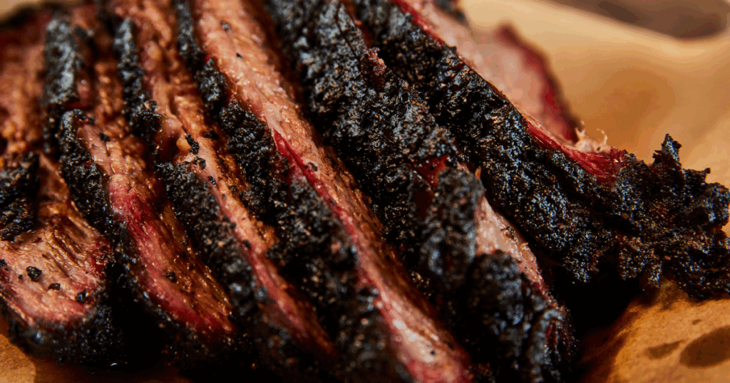 Close-up of perfectly smoked brisket slices with dark bark and juicy pink smoke ring from John Mull’s BBQ catering service