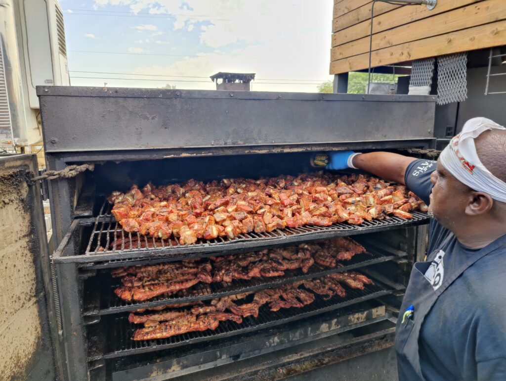Pitmaster loads ribs and rib tips into smoker at John Mull’s Meats for BBQ catering event in Las Vegas