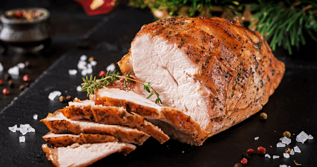 Sliced smoked holiday ham garnished with herbs, ready to serve to holiday guests.