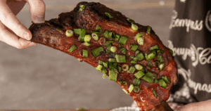 Hand holding a smoked rib tip topped with green onions at John Mull’s Road Kill Grill near North Las Vegas
