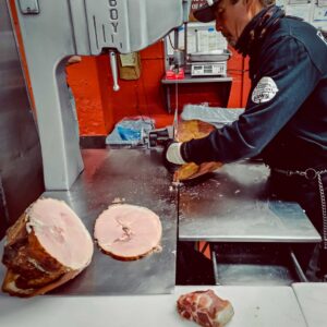 Butcher slicing holiday ham at John Mull’s Meat Market in Las Vegas, preparing slow-smoked meats for Christmas catering and family-style holiday orders.