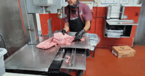 Butcher using a band saw to cut fresh meat and beef at John Mull’s Meats, a trusted Las Vegas butcher shop known for quality cuts.