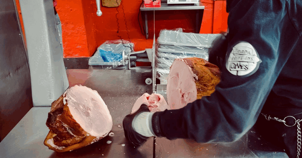 Butcher slicing smoked ham at John Mull’s Meats in Las Vegas, showcasing traditional preparation and award winning meat shop market craftsmanship.