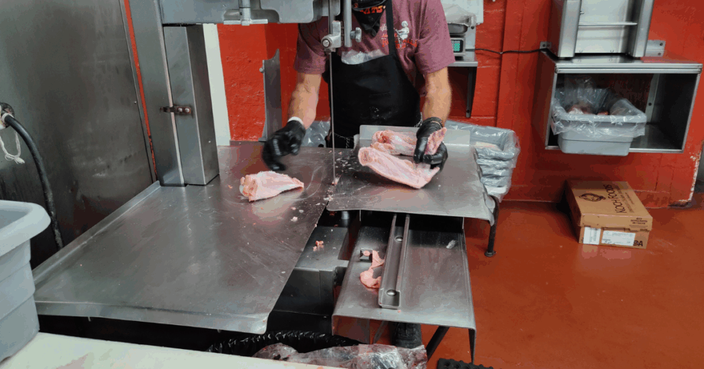 Butcher cutting fresh pork by hand at John Mull’s Meats butcher counter in Las Vegas, showcasing professional meat preparation and local craftsmanship