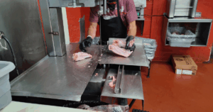 Butcher cutting fresh pork by hand at John Mull’s Meats butcher counter in Las Vegas, showcasing professional meat preparation and local craftsmanship