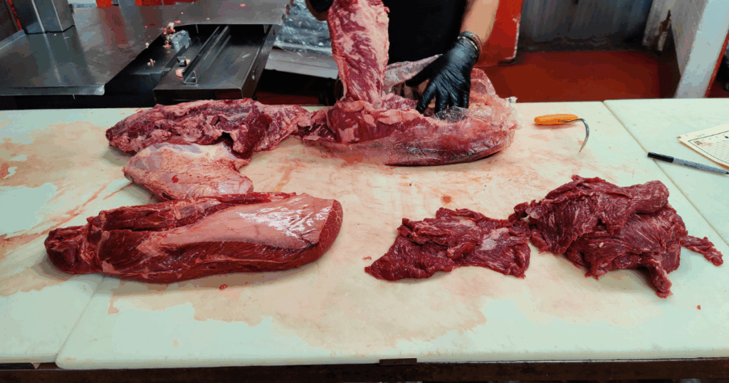 Owner and professional butcher hand-cutting fresh beef at John Mull’s Meats in Las Vegas, showcasing expert butchery and high-quality meat preparation