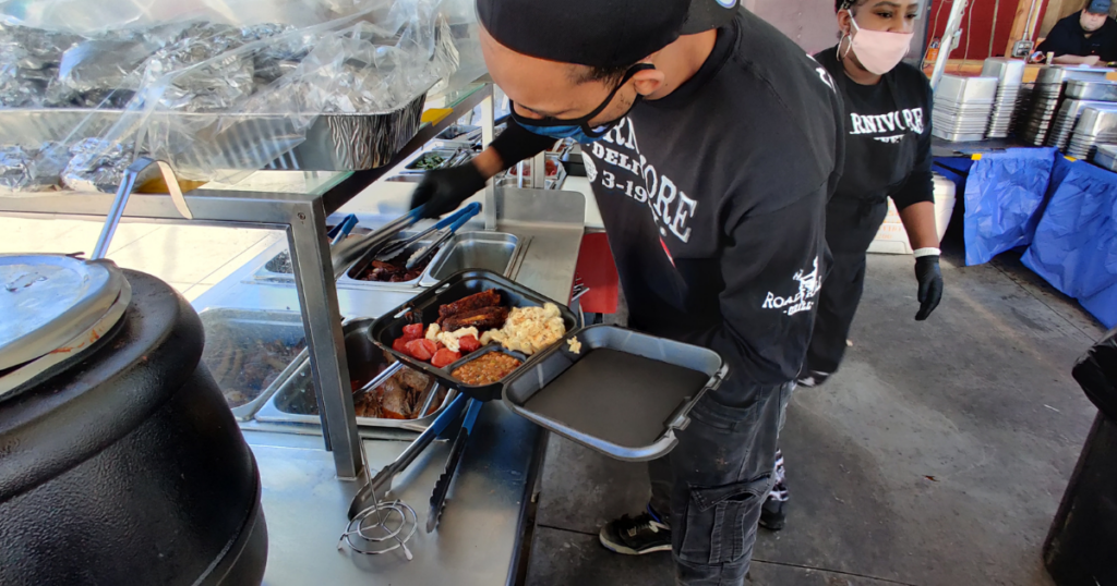 Road Kill Grill staff preparing a BBQ plate with smoked meats and homestyle sides for outdoor dining in Las Vegas.