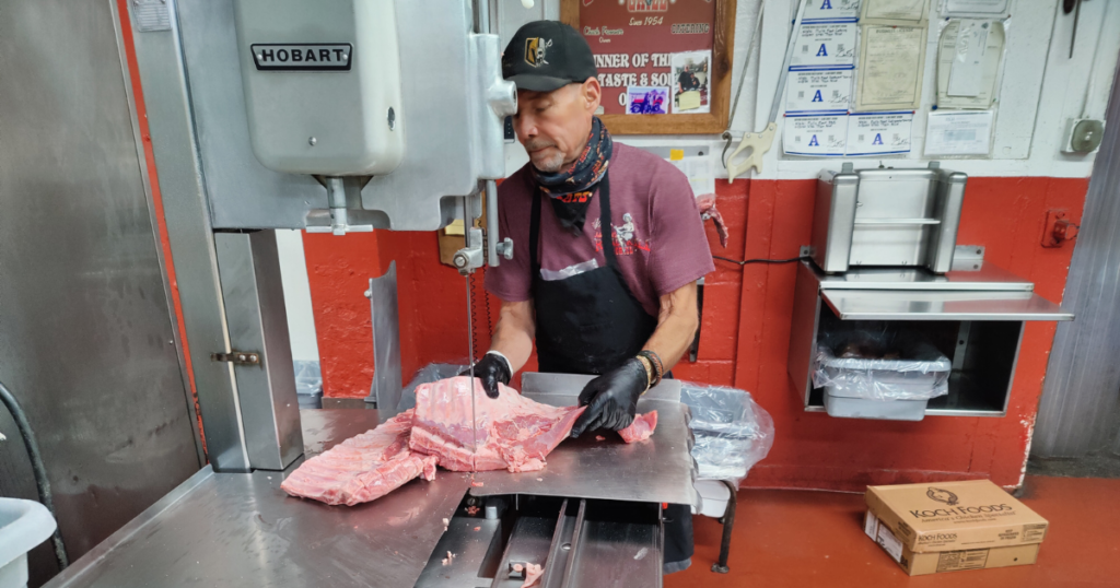 Professional butcher preparing premium beef cuts at a Las Vegas meat market using a commercial meat saw at John Mull's Meats.